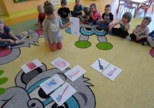 Dziewczynka unosi ilustrację przedstawiającą lusterko, w tle siedzą dzieci.